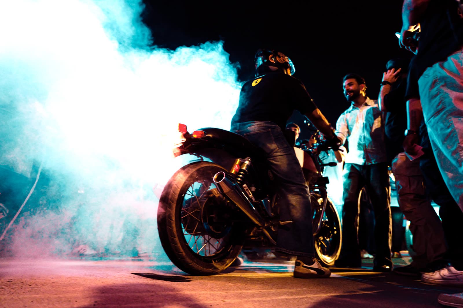 Motorcycle burnout with coloured smoke in front of a night crowd